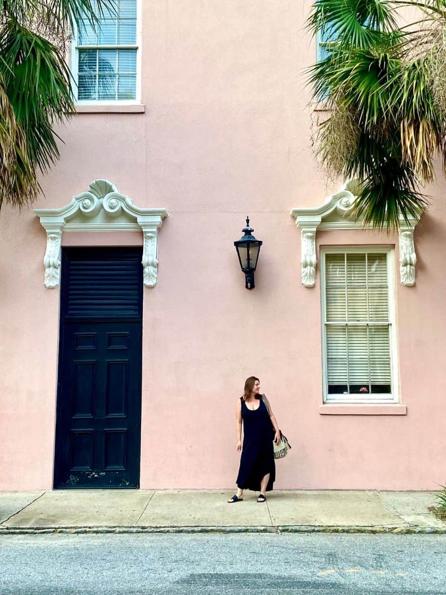A Solo Woman standing in front of a pink building Traveling in Charleston