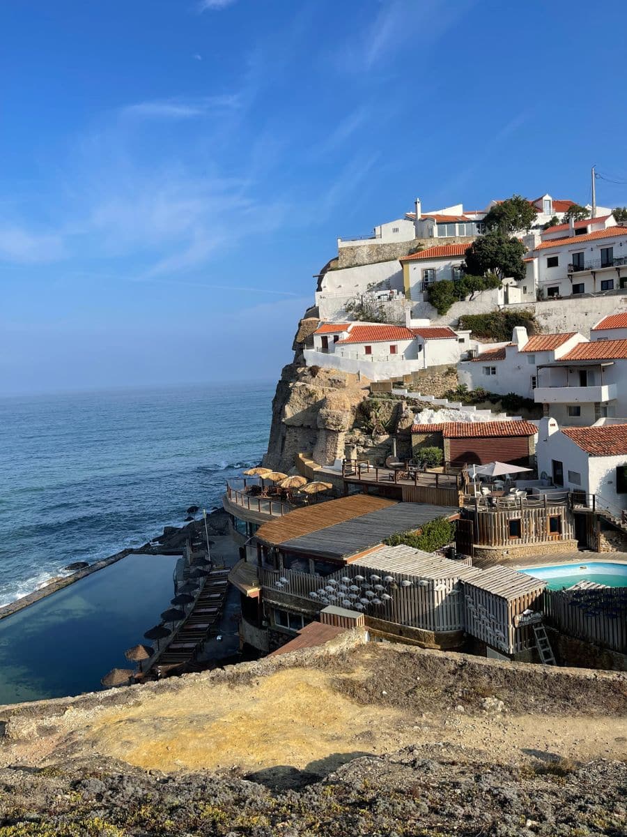 Charming white houses with terracotta rooftops perched on cliffs, overlooking the tranquil ocean pool at Azenhas do Mar.