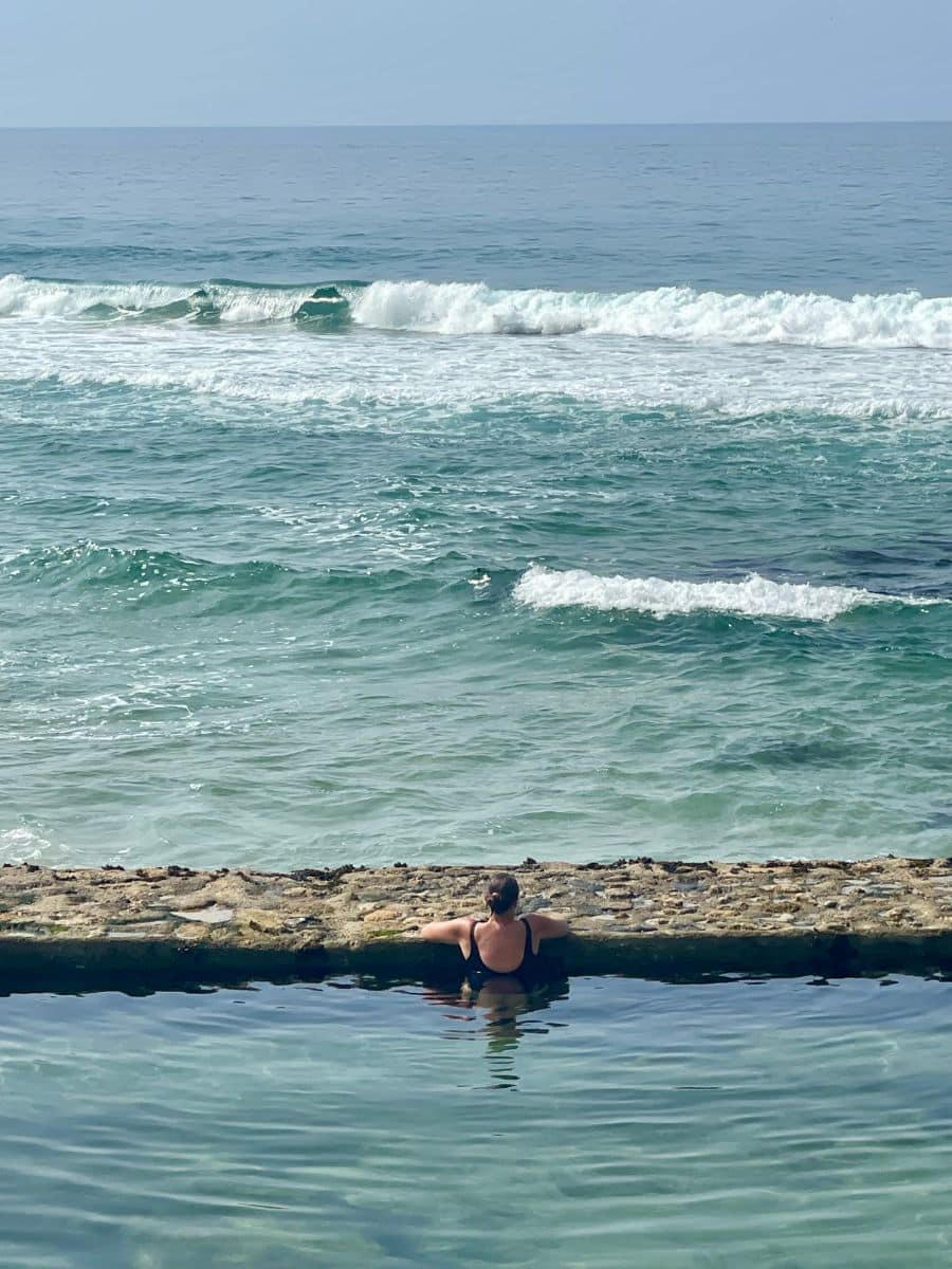A woman peacefully relaxing in the serene ocean pool at Azenhas do Mar, facing the gentle waves of the Atlantic.