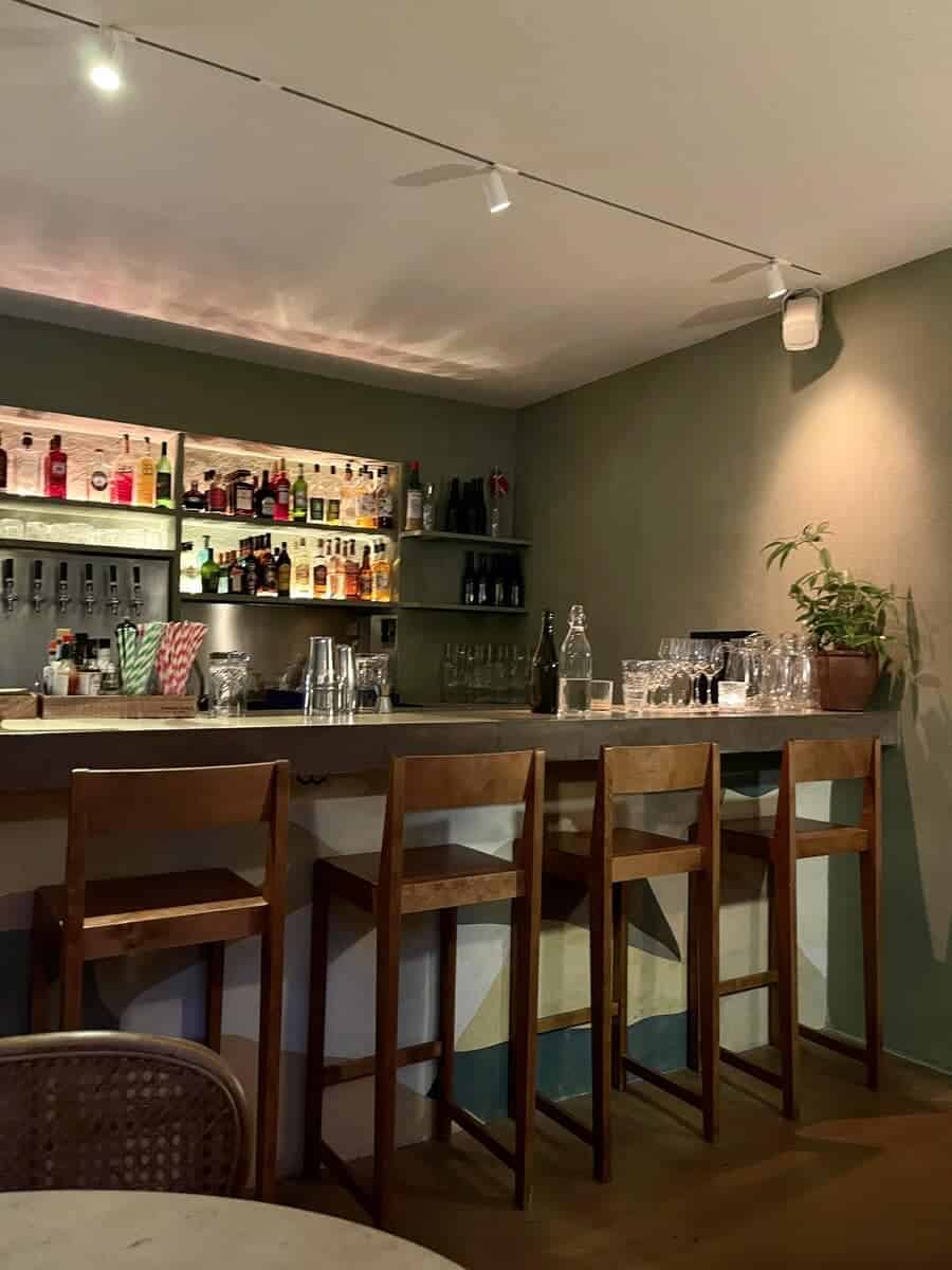 Interior of Yaffa in Copenhagen showing a cozy bar setting with wooden stools, a well-stocked bar with various bottles, and a green plant adding a touch of freshness.