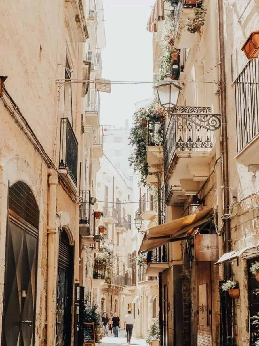 Charming narrow street in Bari, Italy, lined with traditional balconies, blooming flowers, and rustic stone buildings, capturing the essence of southern Italian architecture.