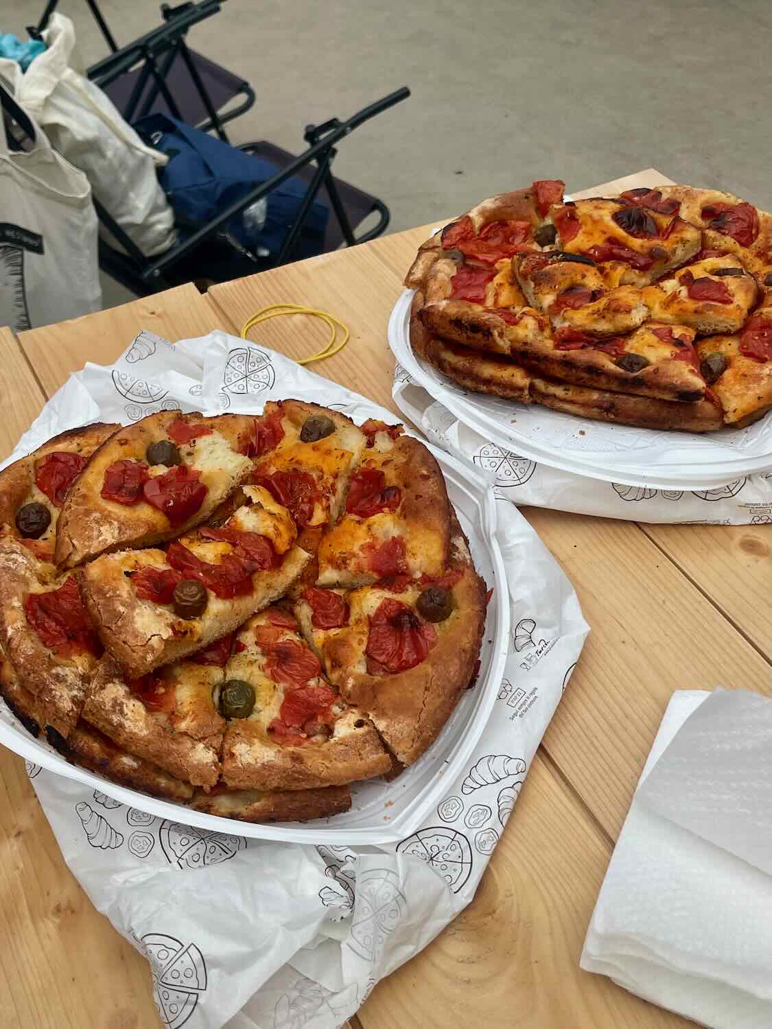 Traditional Focaccia Barese served on paper plates, topped with fresh tomatoes, olives, and a drizzle of olive oil, capturing the flavors of Bari, Italy.