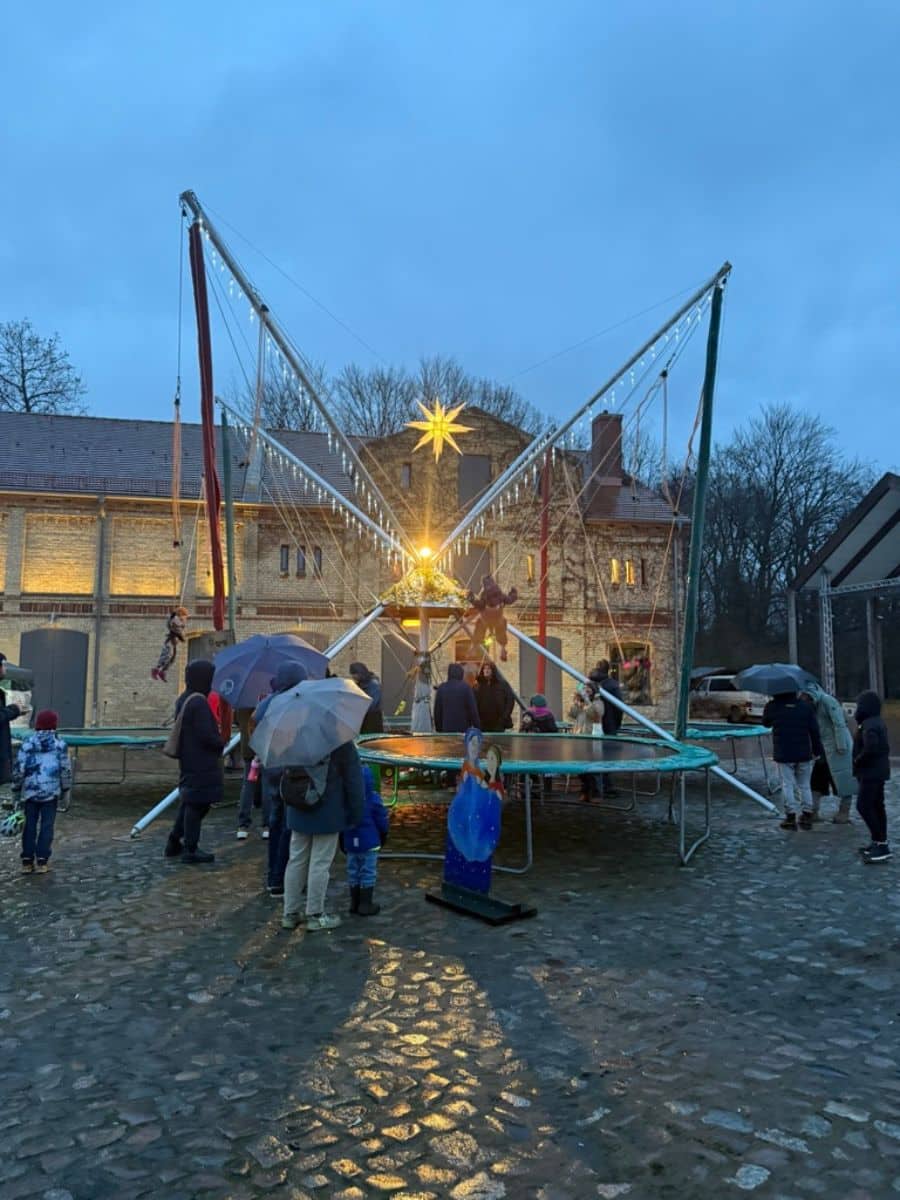 A festive trampoline setup with children enjoying activities under a large glowing star, surrounded by the castle's rustic buildings and cobblestone paths.