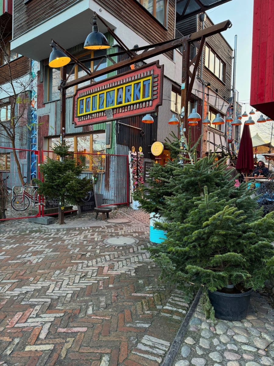 The vibrant entrance to Holzmarkt, adorned with colorful signs and surrounded by small evergreen trees, creating a cheerful holiday atmosphere.