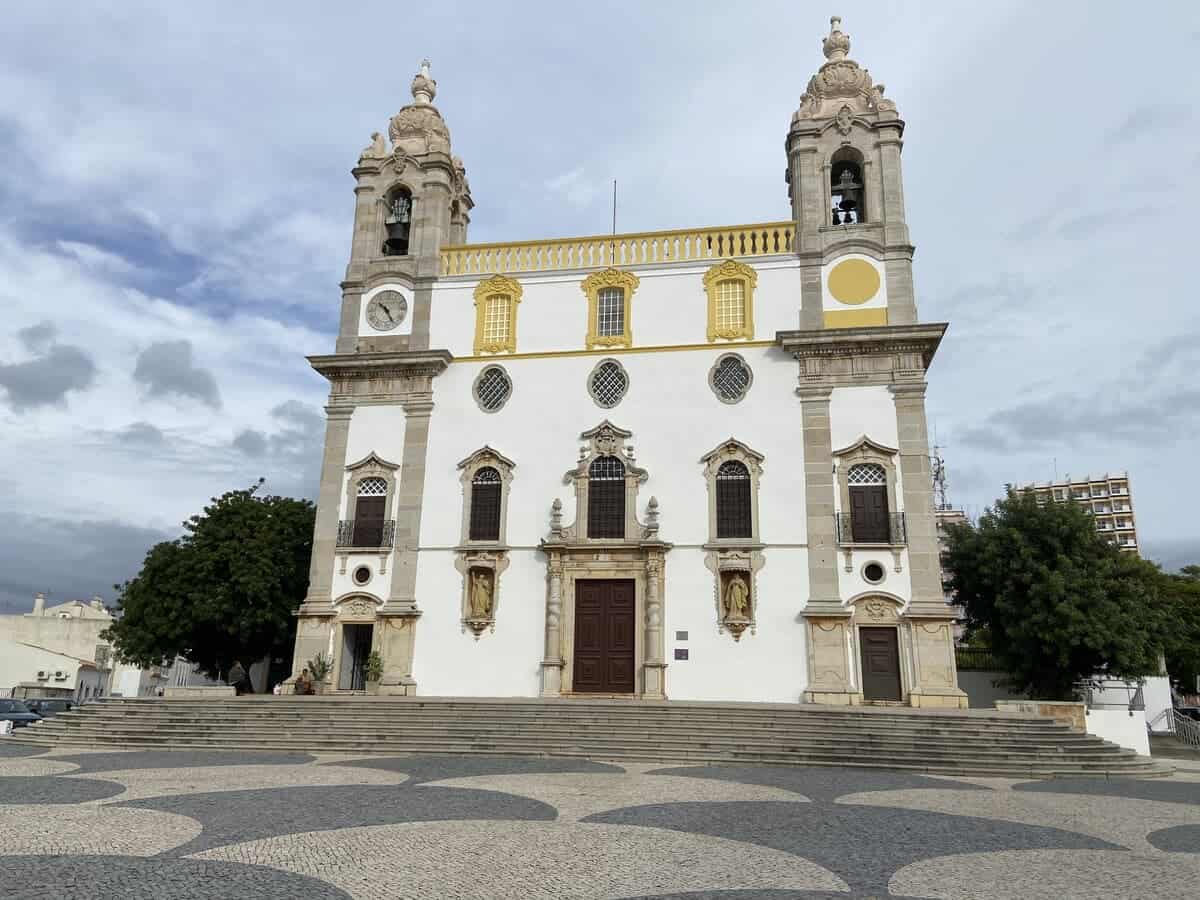 Historic Carmo Church (Igreja do Carmo) in Faro, Portugal, under a cloudy sky, with distinctive Portuguese pavement in the foreground. A perfect representation of solo travel Faro, highlighting the city's rich architecture and tranquil atmosphere.