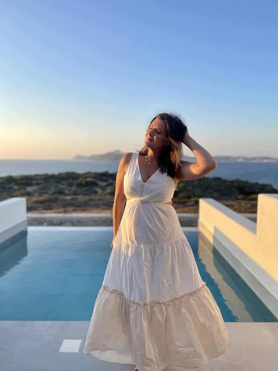 A woman standing in front of a pool with a beautiful sunset in the background