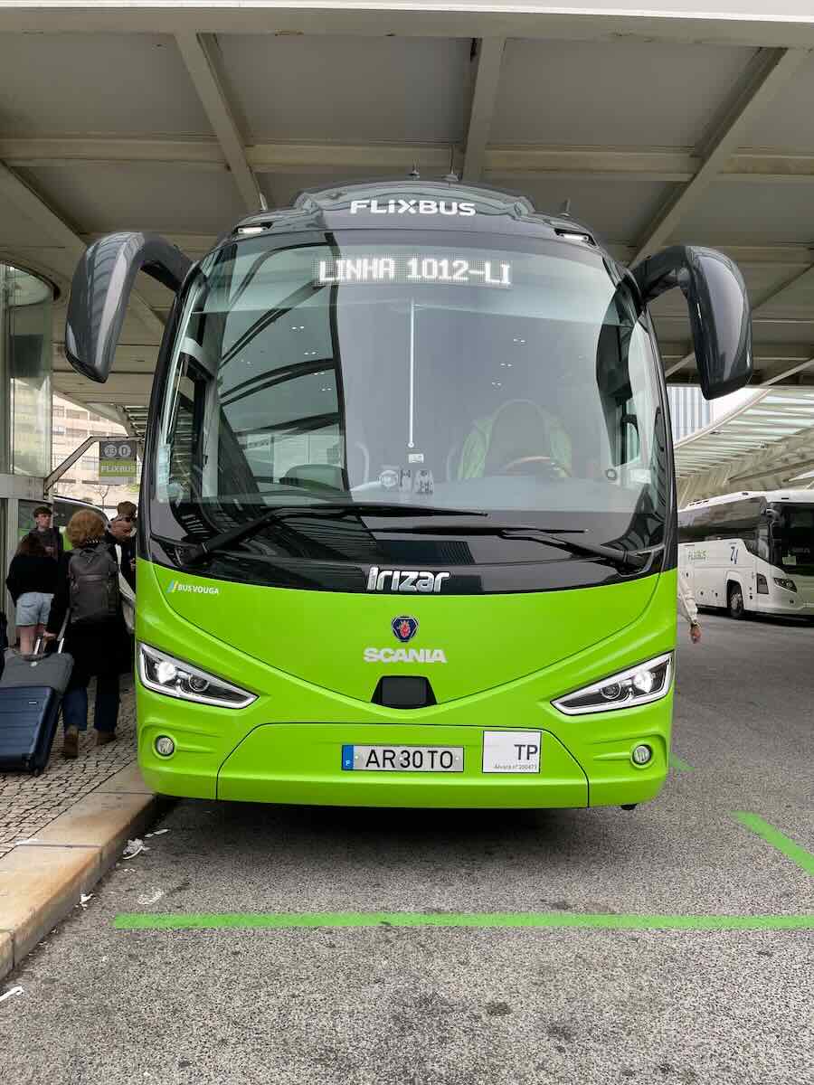 A green FlixBus parked at a bus terminal with passengers nearby.