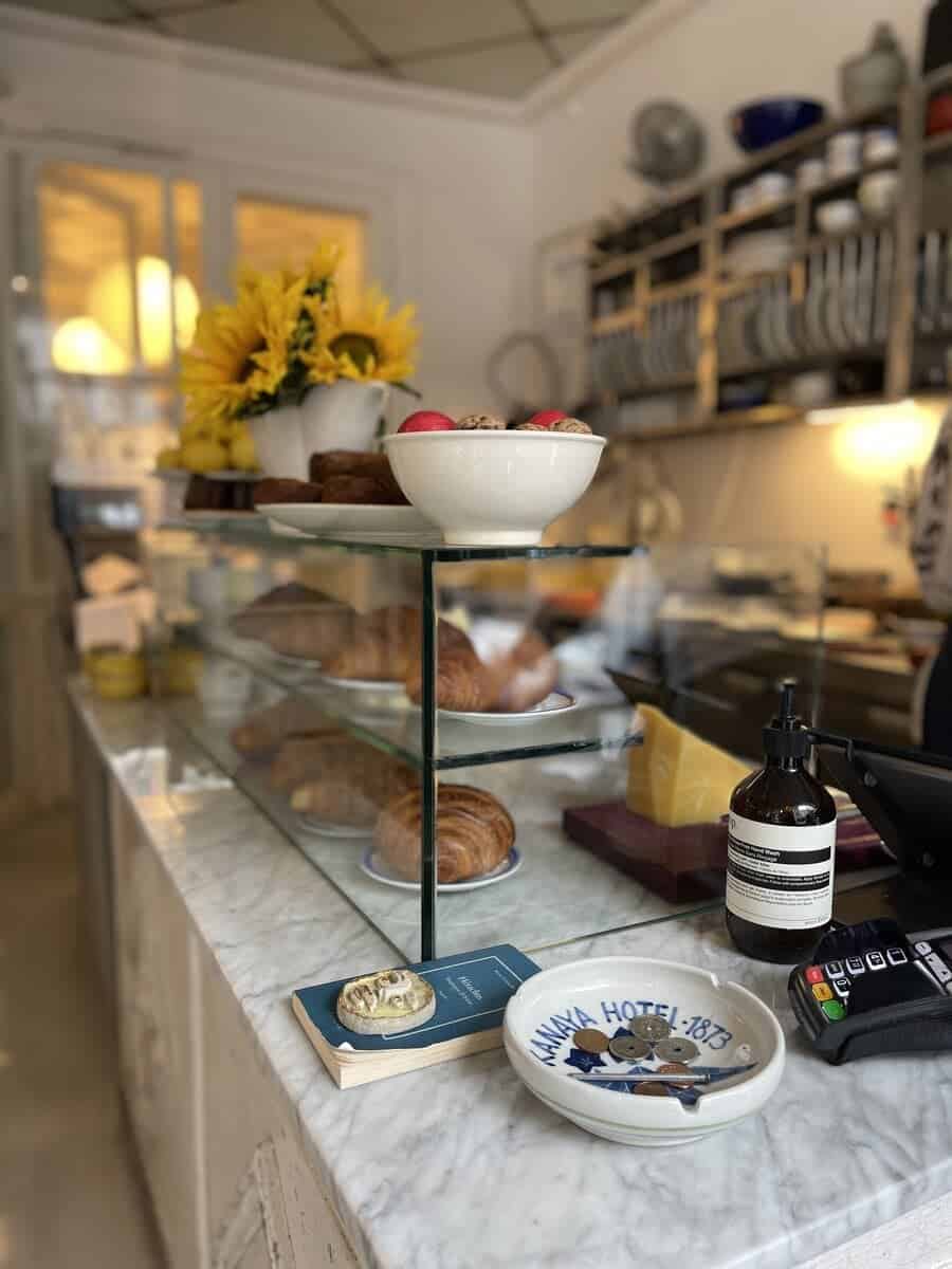 Charming interior of Café Atelier September with a focus on a marble counter displaying assorted pastries, a bowl of fruits, and sunflowers adding a burst of color, giving a glimpse of the cozy café ambiance.