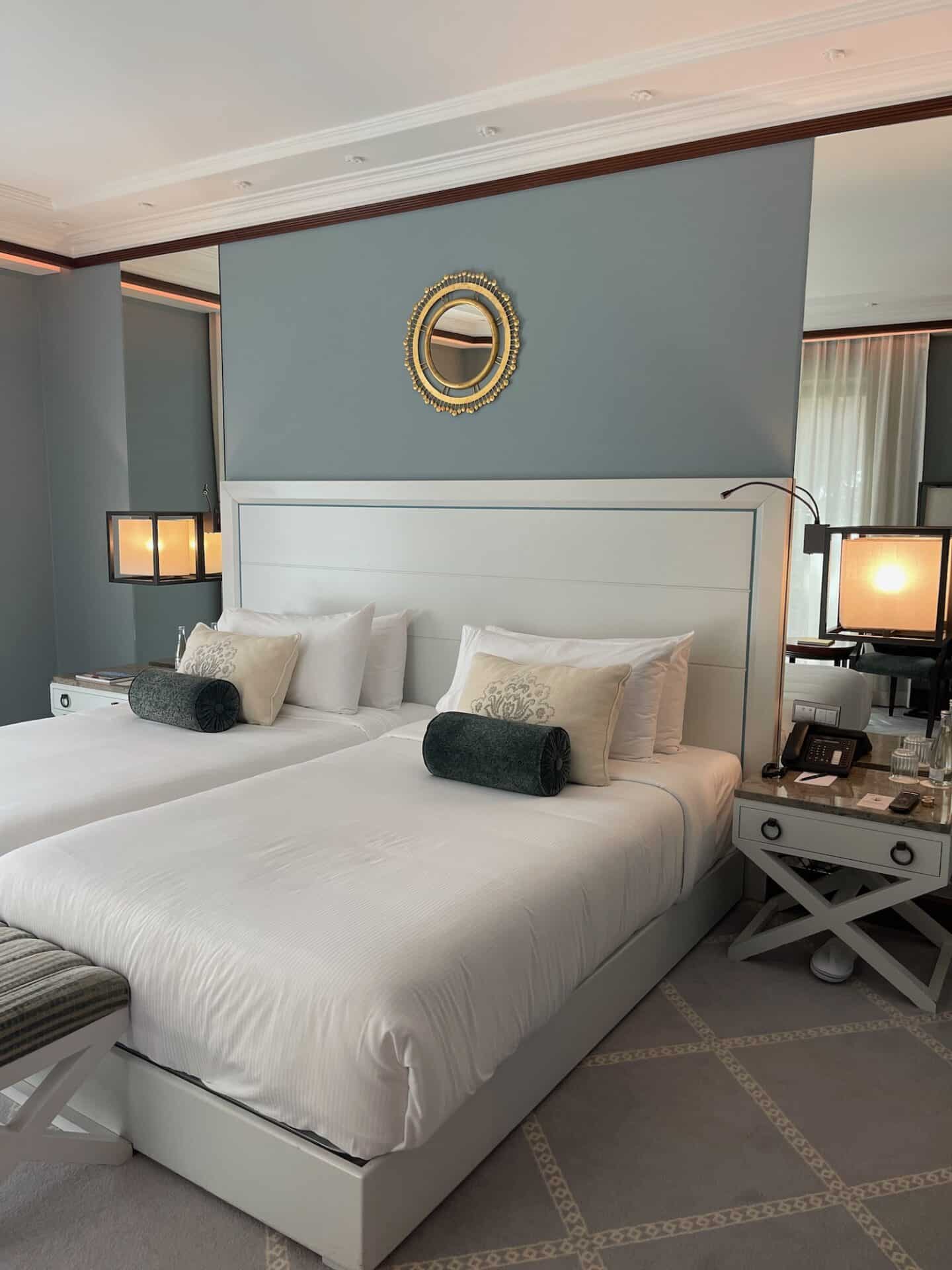 Elegant hotel room with two neatly made twin beds, modern gray and white decor, soft lighting, and stylish accents for a cozy and relaxing atmosphere.