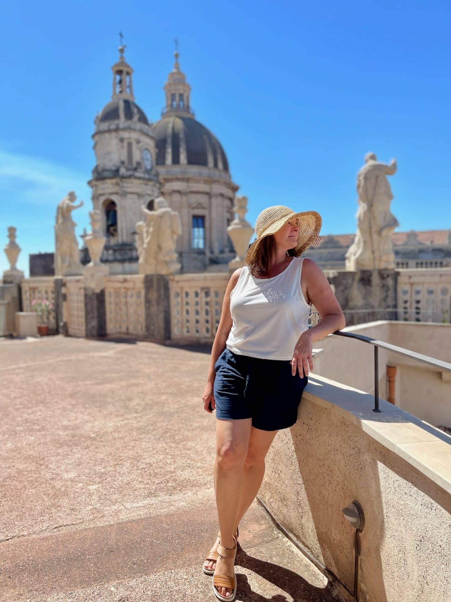 Solo traveler enjoying a sunny day on the rooftop of Catania Cathedral in Italy, with the stunning baroque domes and statues framing the vibrant blue sky.