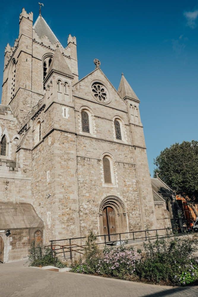 The majestic facade of a medieval church in Dublin, showcasing intricate stone carvings and a large rose window, set against a bright blue sky, a sight to behold for history enthusiasts traveling alone.