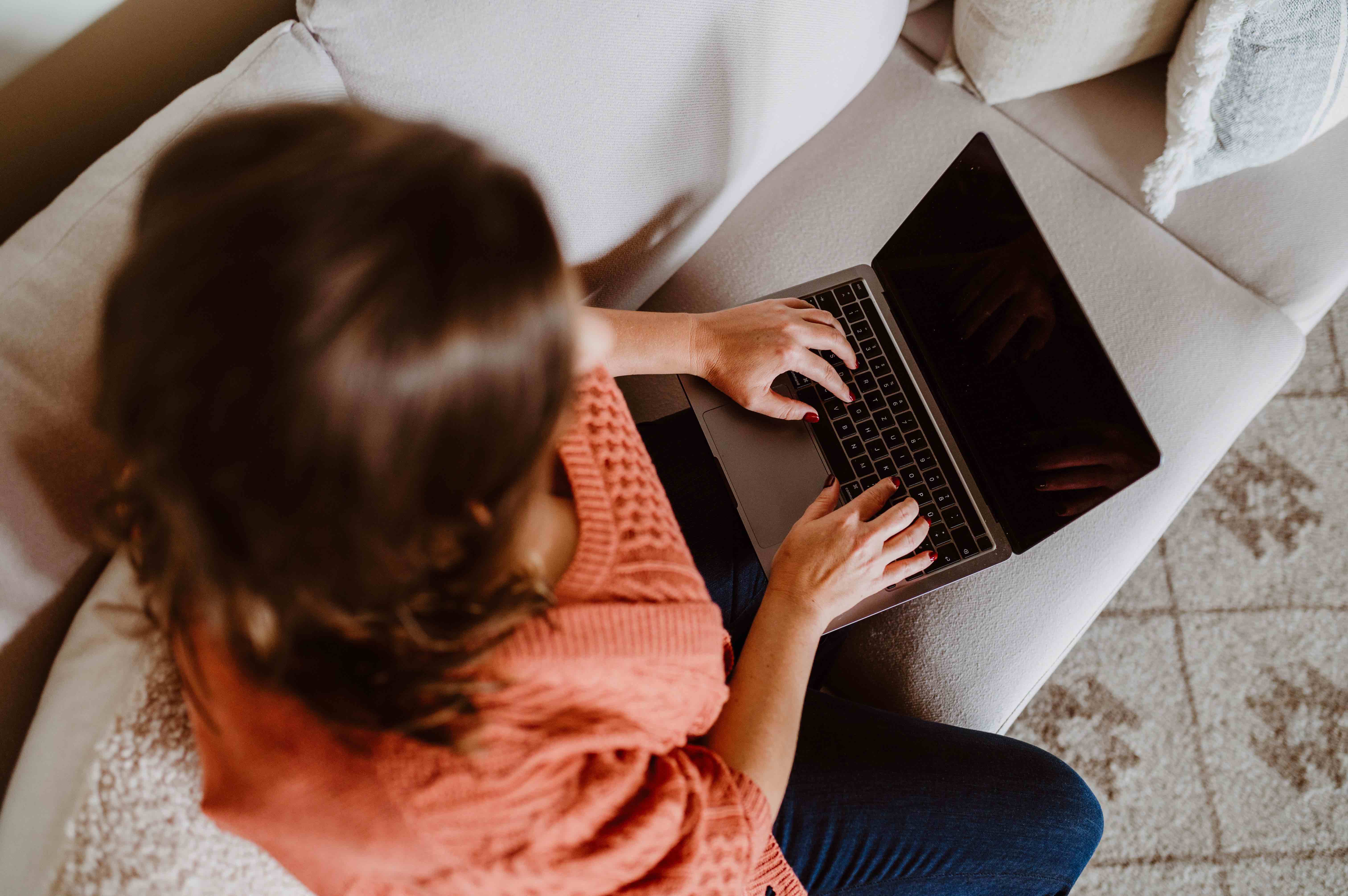 Solo female traveler researching destinations using ChatGPT for travel planning on a laptop, seated on a cozy couch.