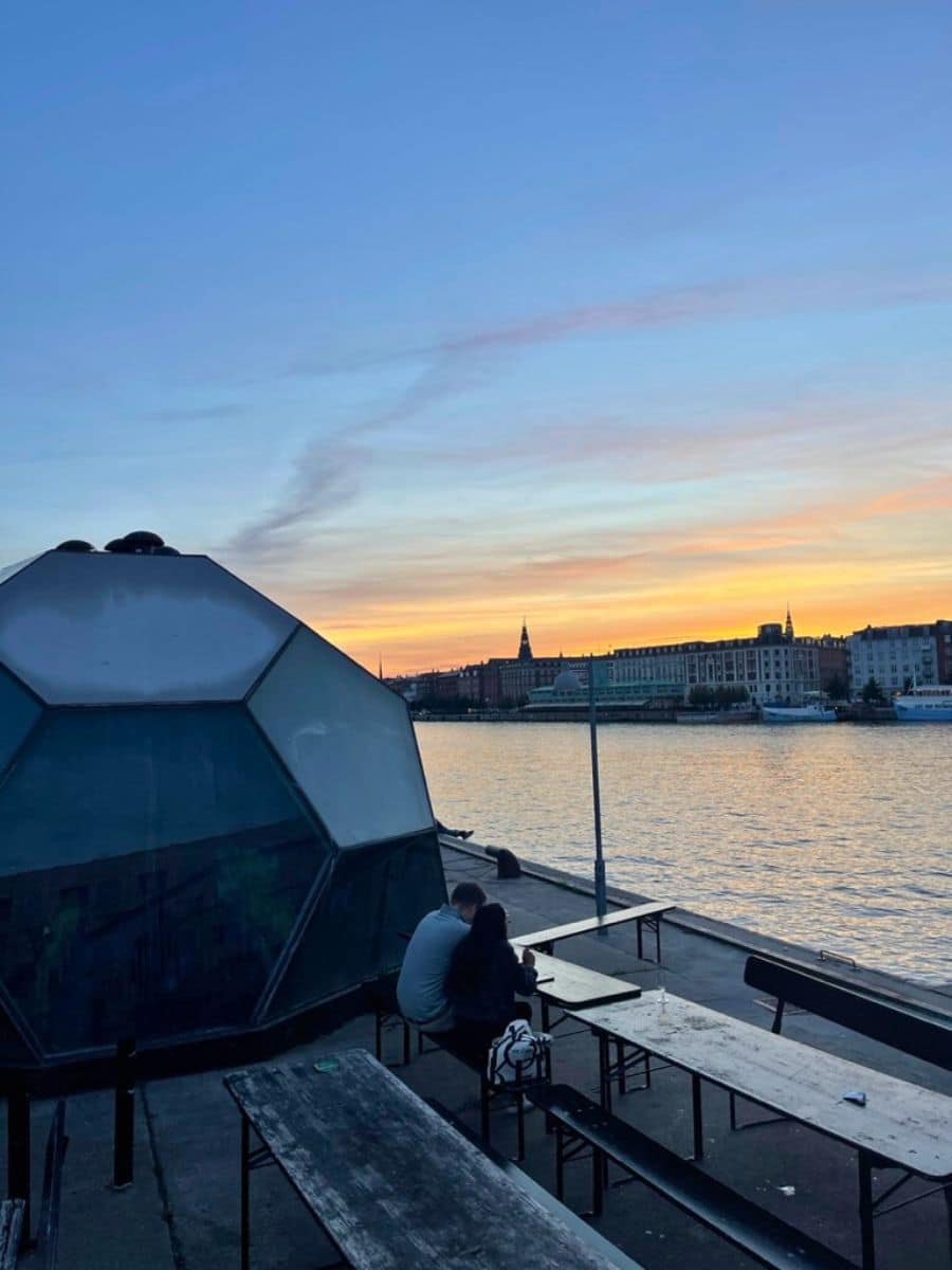 A couple seated at a waterfront dining area in Copenhagen during sunset, showcasing the romantic and relaxed outdoor culture of the city.