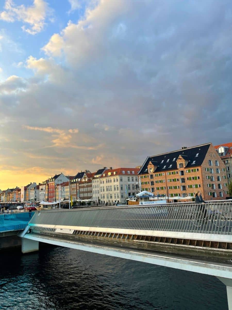 Sunset view over a bridge in Copenhagen with pastel-colored buildings lining the river, reflecting the city's vibrant yet calm evening atmosphere.