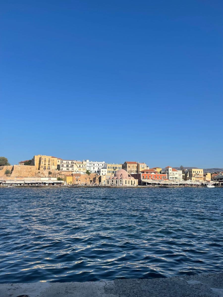 Picturesque waterfront view of colorful Venetian-style buildings and calm blue waters in Chania, Crete, offering a charming urban coastal scene.