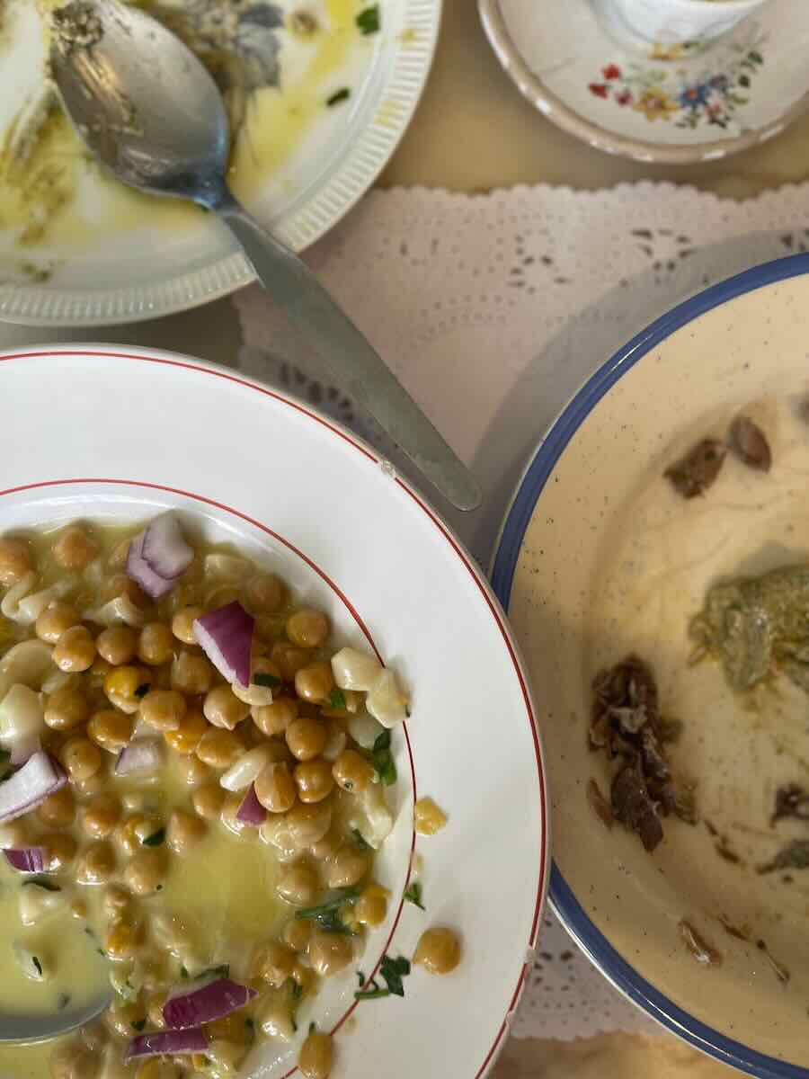 A plate of chickpeas with onion and herbs, and a bowl of creamy dip with bread, both partially eaten.