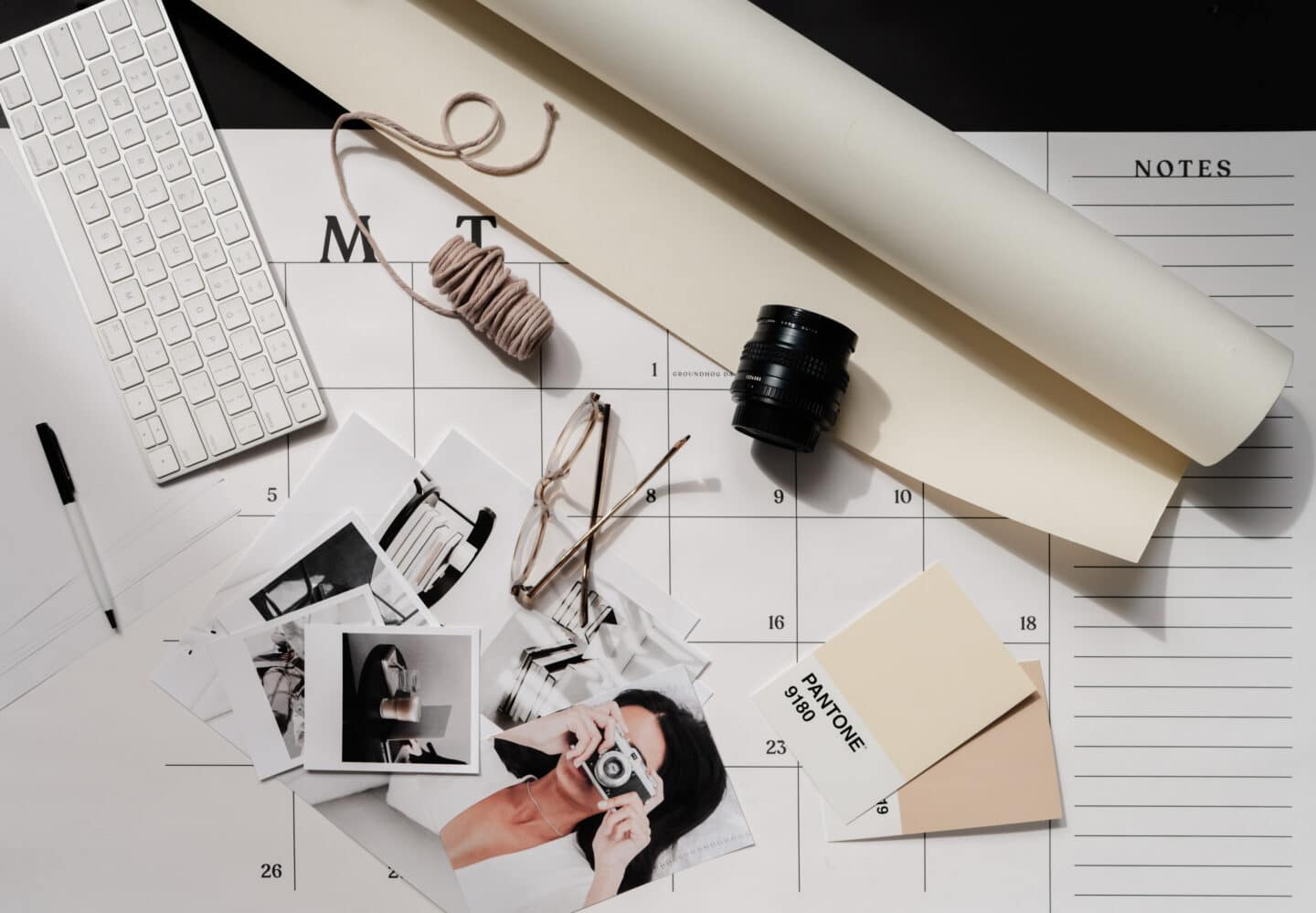 A creative workspace featuring a calendar, keyboard, camera lens, glasses, and photography prints, giving off an aesthetic and organized vibe.