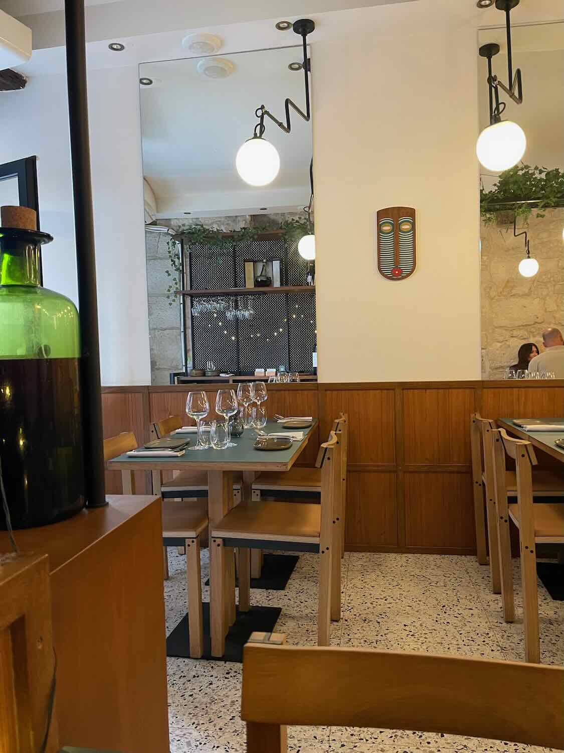 A view inside Hébé restaurant in Paris, characterized by its modern yet welcoming design. The dining area is calm with natural wood furniture, terrazzo flooring, and stylish globe lighting, ready to host diners in a casual, chic setting.