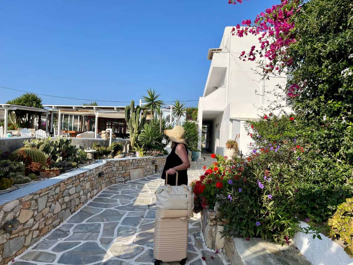 A woman and her suitcase manifesting travel to a greek island village surround by flowers
