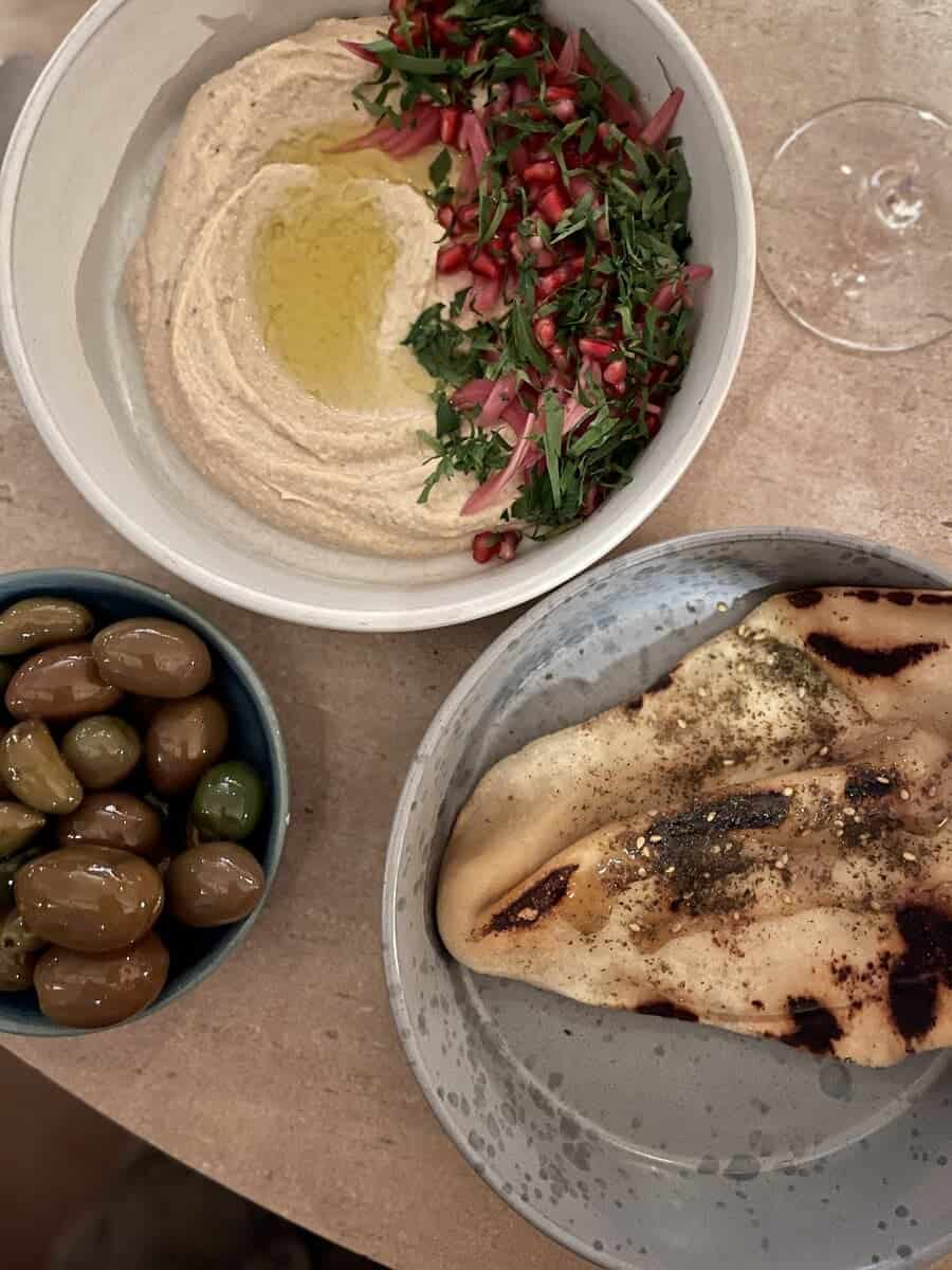 A Mediterranean spread at Yaffa in Copenhagen featuring a large bowl of creamy hummus with olive oil, a plate of vibrant chopped salad with pomegranate seeds, freshly baked flatbread with za'atar, and a bowl of green olives.