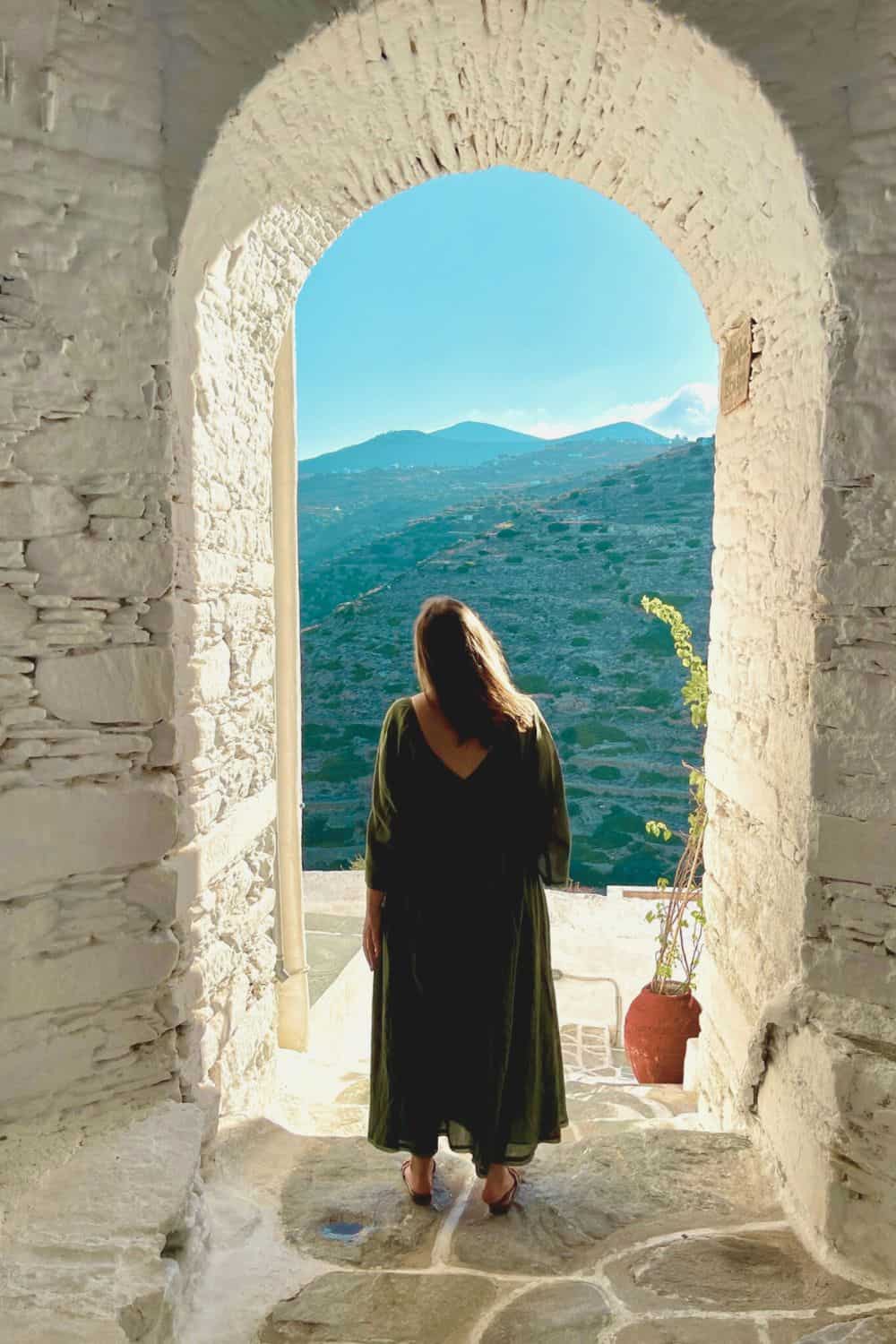 A woman traveling solo standing in a door way looking out at the mountains. 