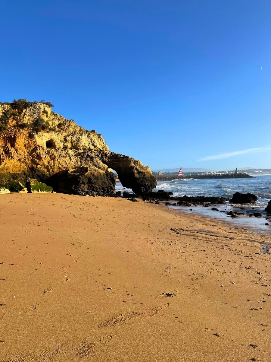 Scenic beach in Lagos with a natural rock arch formation and calm waves under a bright blue sky.