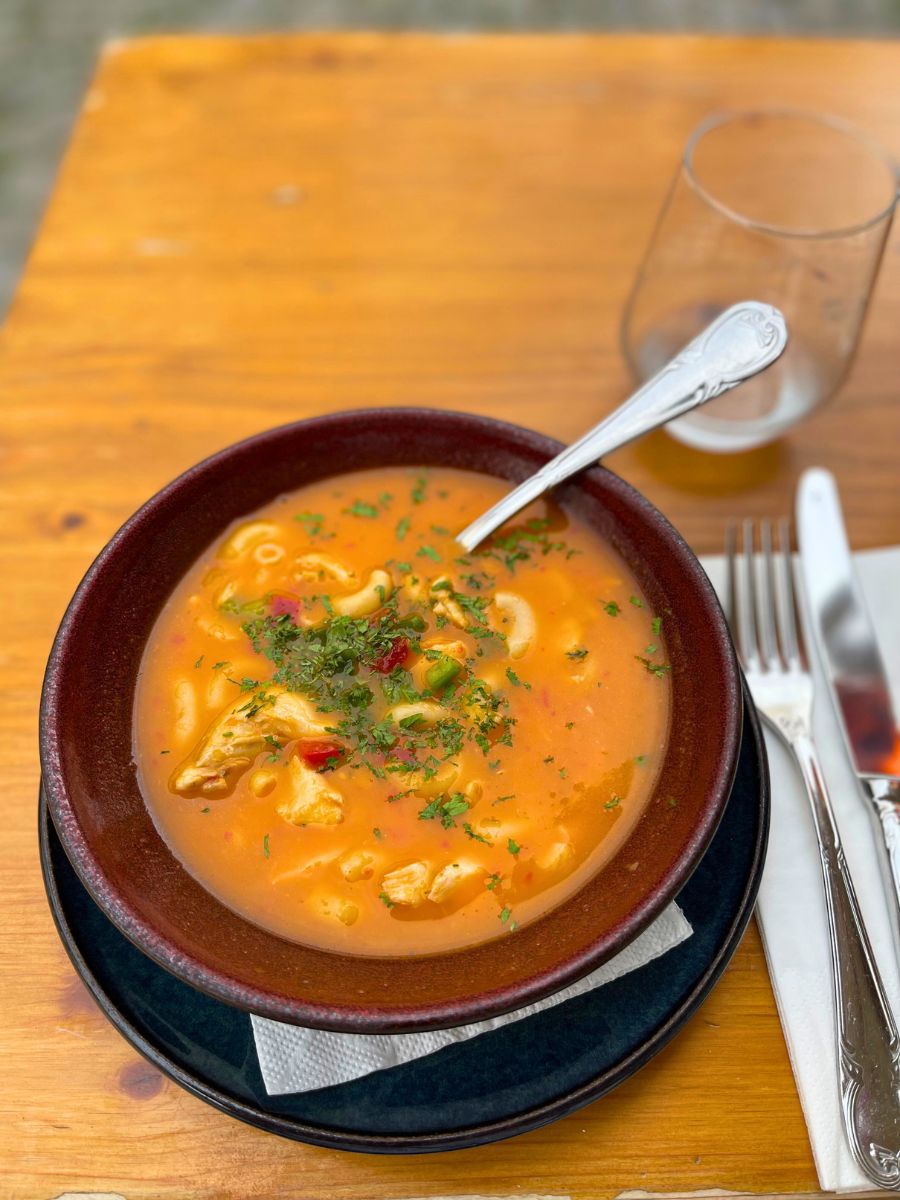 Bowl of traditional Portuguese fish soup with pasta and herbs, served outdoors on a wooden table