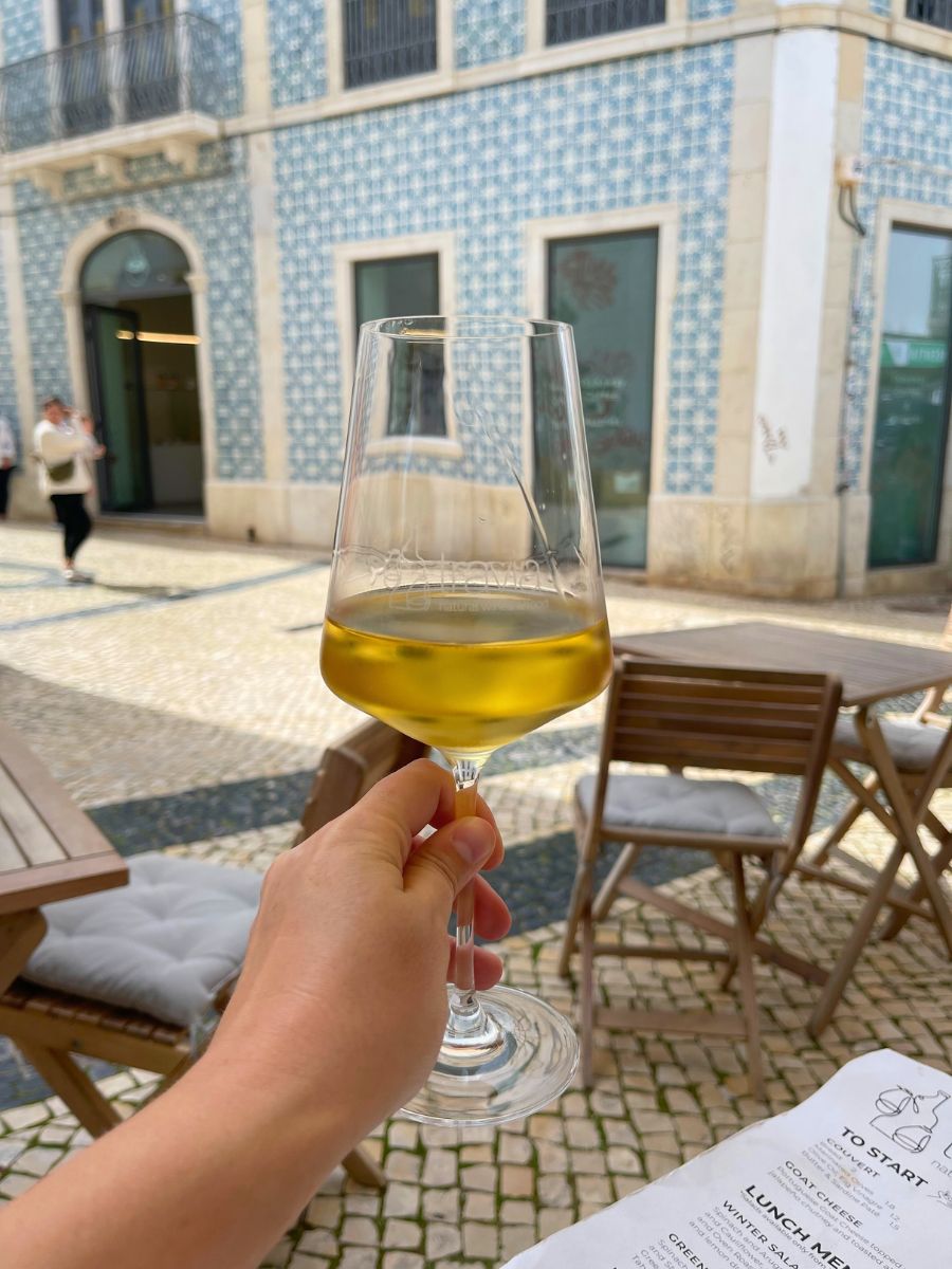 Glass of Portuguese white wine held up on a sunny terrace in Faro, with a blue-tiled building in the background