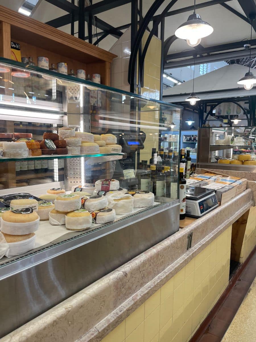 Cheese display at a deli counter with various types of cheeses and breads.