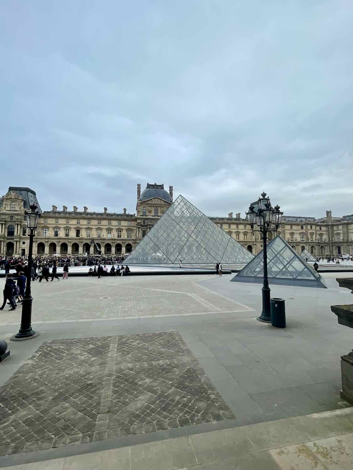 The iconic Louvre Museum with its modern glass pyramid contrasted against the historical building facade, under a cloudy sky, a classic sight in the heart of Paris.