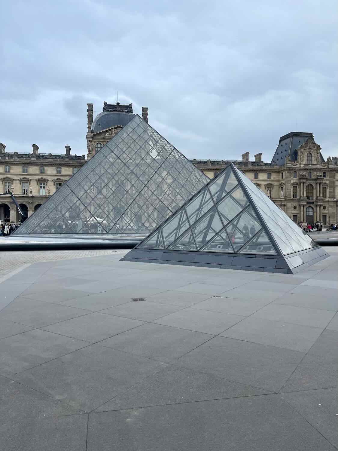 A close-up view of the Louvre's glass pyramid, showcasing its geometric design and the reflection of the surrounding historical architecture, symbolizing the blend of old and new in Paris.