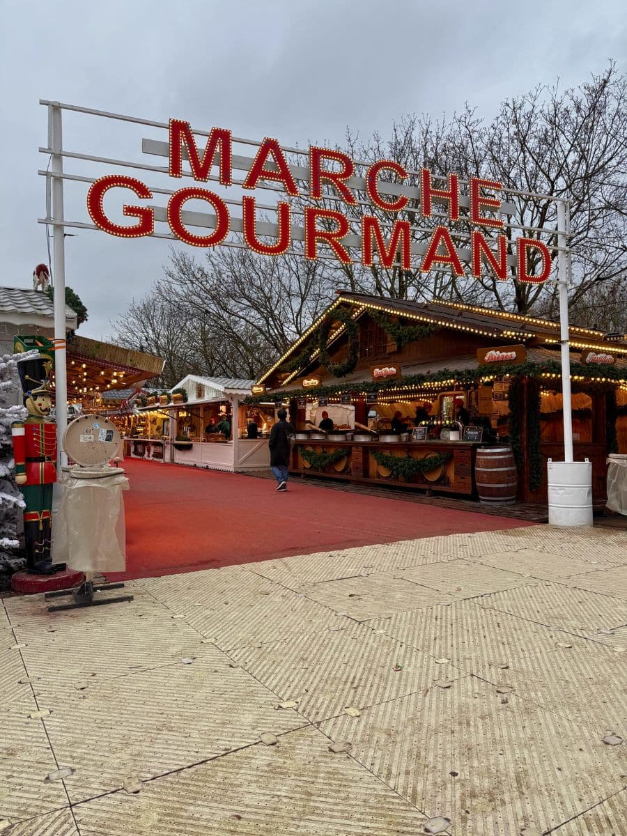 Close-up view of the 'Marche Gourmand' entrance at the Paris Christmas market, showcasing brightly lit signage, festive stalls, and decorative elements.