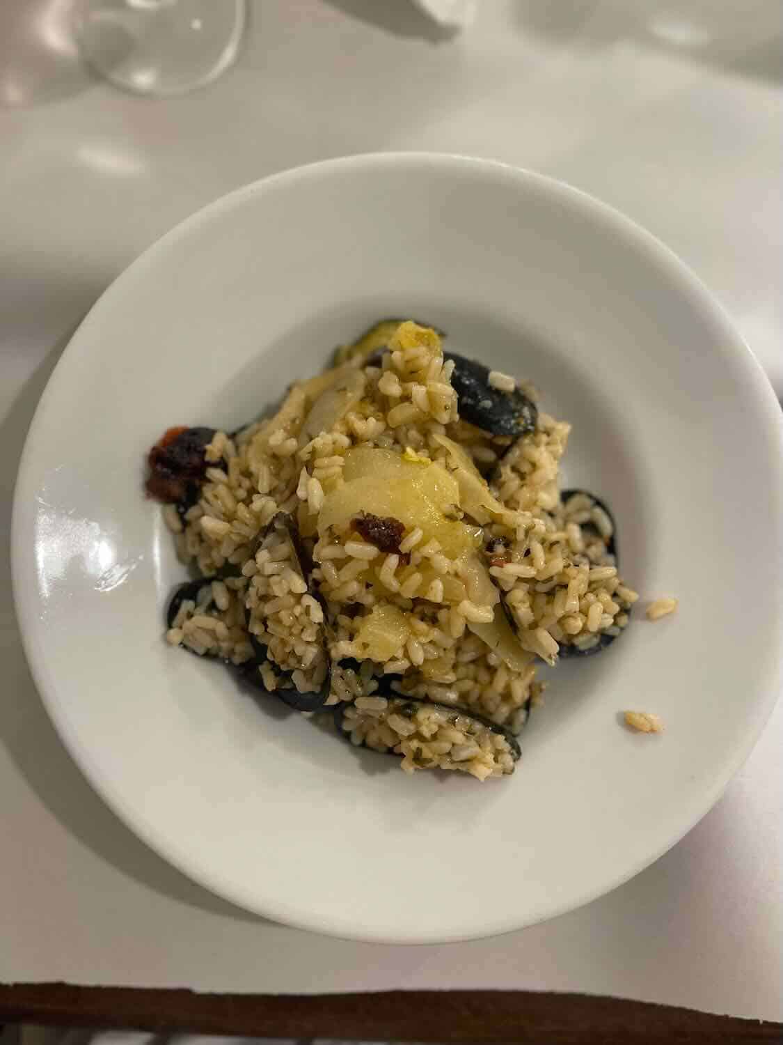 A bowl of rice and mussels served in Bari, Italy. The dish includes mussels, rice, and vegetables, and is presented on a white plate with a simple, rustic appeal.