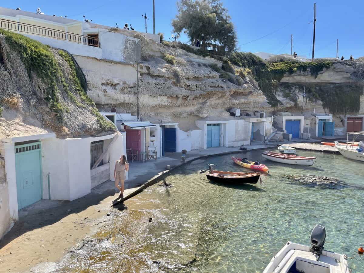 A female traveler alone in Milos Island walking by the little colored doors of the storage units by the sea. 
