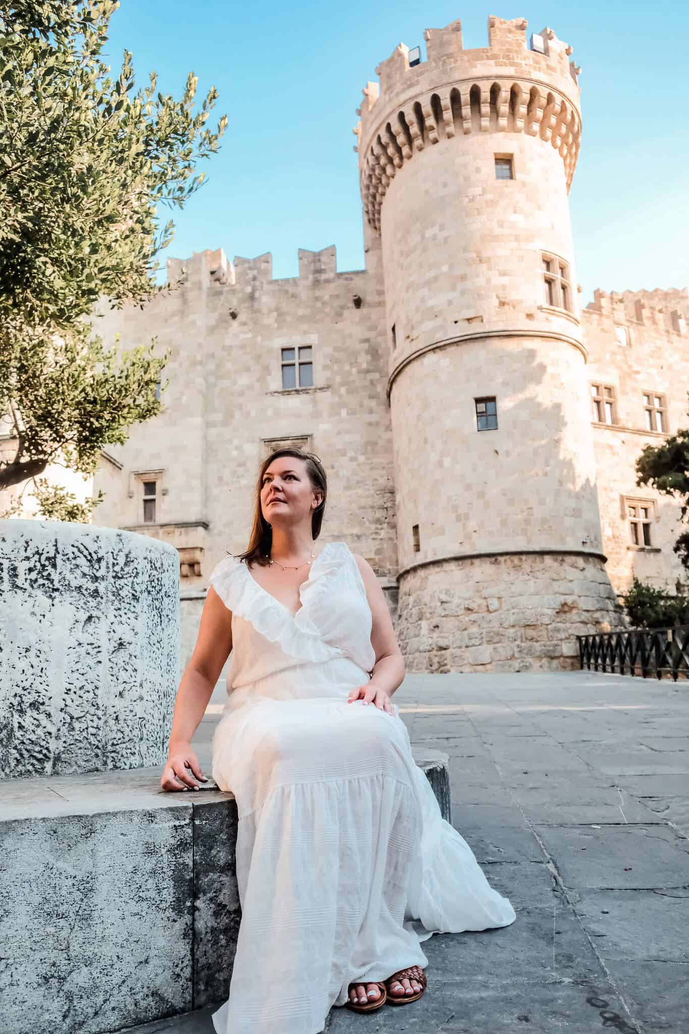 Sitting on a stone bench outside the City Wall Gates in Rhodes, Greece, one of the stops on my Rhodes itinerary for solo females.