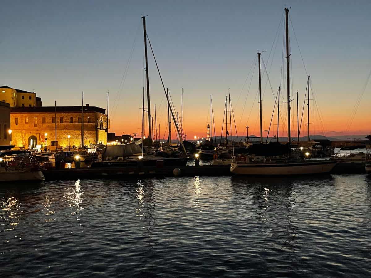 Sunsets of orange and red in the Chania Harbor. Several sail boats in the water. 