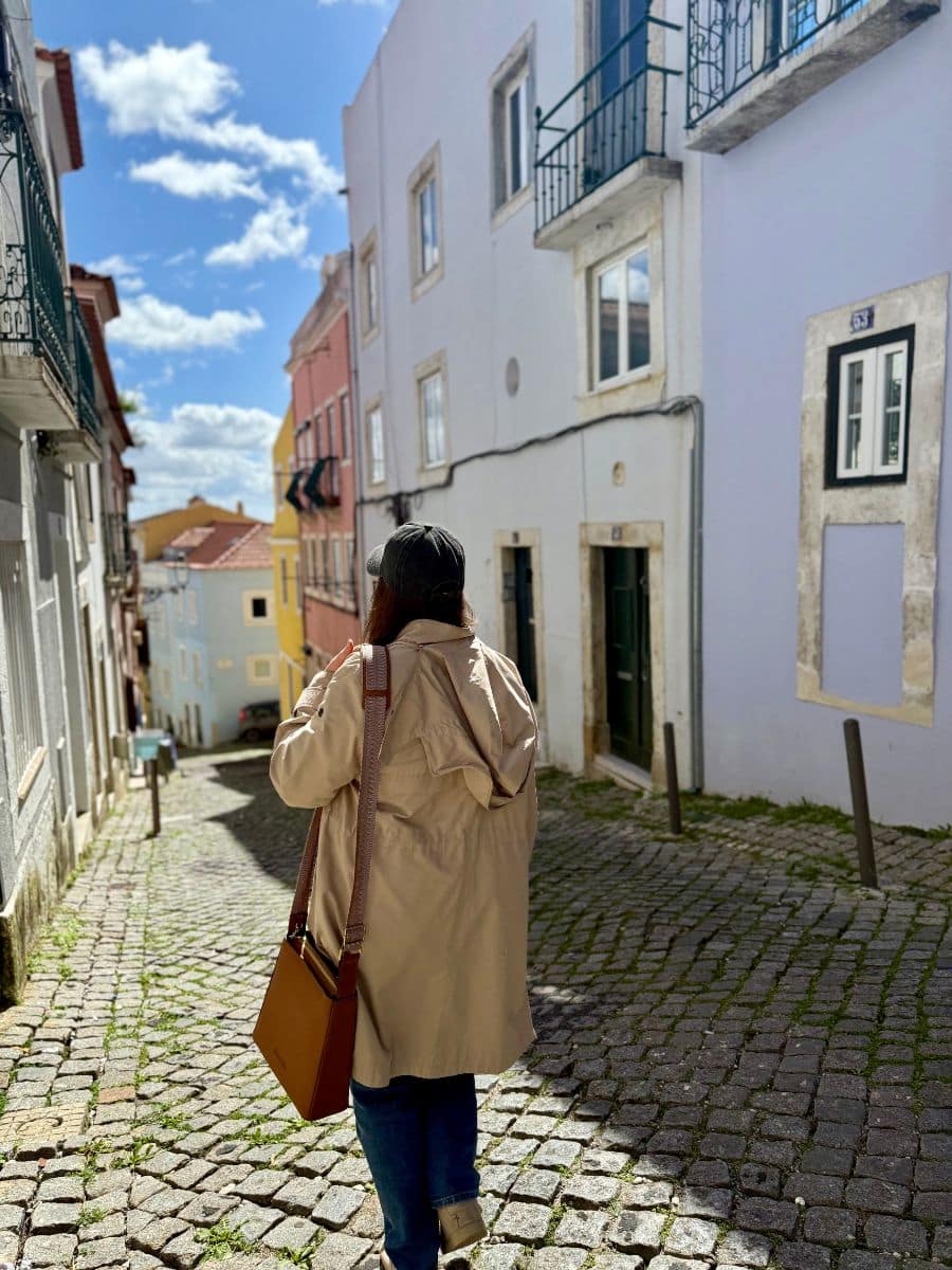 Woman walking down a charming cobblestone street with a brown antitheft crossbody purse.