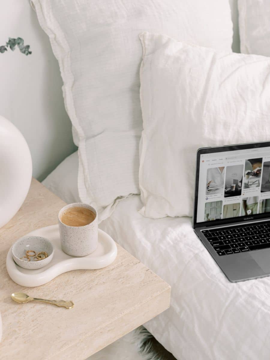 Cozy bed setup with coffee and laptop showing Pinterest—perfect inspiration for trip planning with an aesthetic Notion travel template.