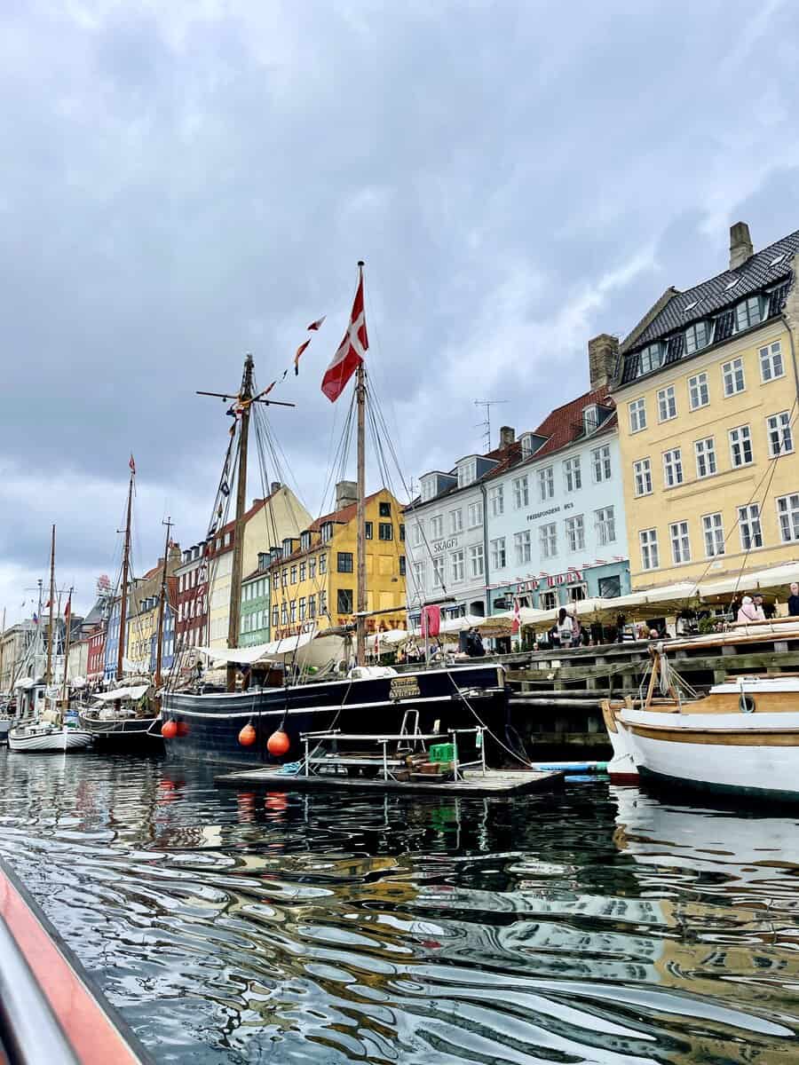 Vibrant scene at Copenhagen's Nyhavn, featuring colorful buildings and a bustling waterfront lined with boats, under an overcast sky.