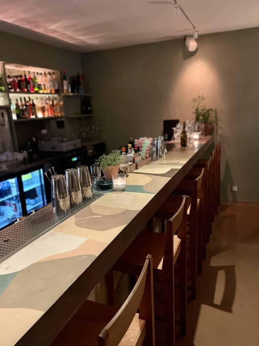 A view of Yaffa’s bar in Copenhagen with a unique tiled counter in pastel colors, featuring numerous glasses ready for service and several small potted plants, creating a welcoming and stylish atmosphere.