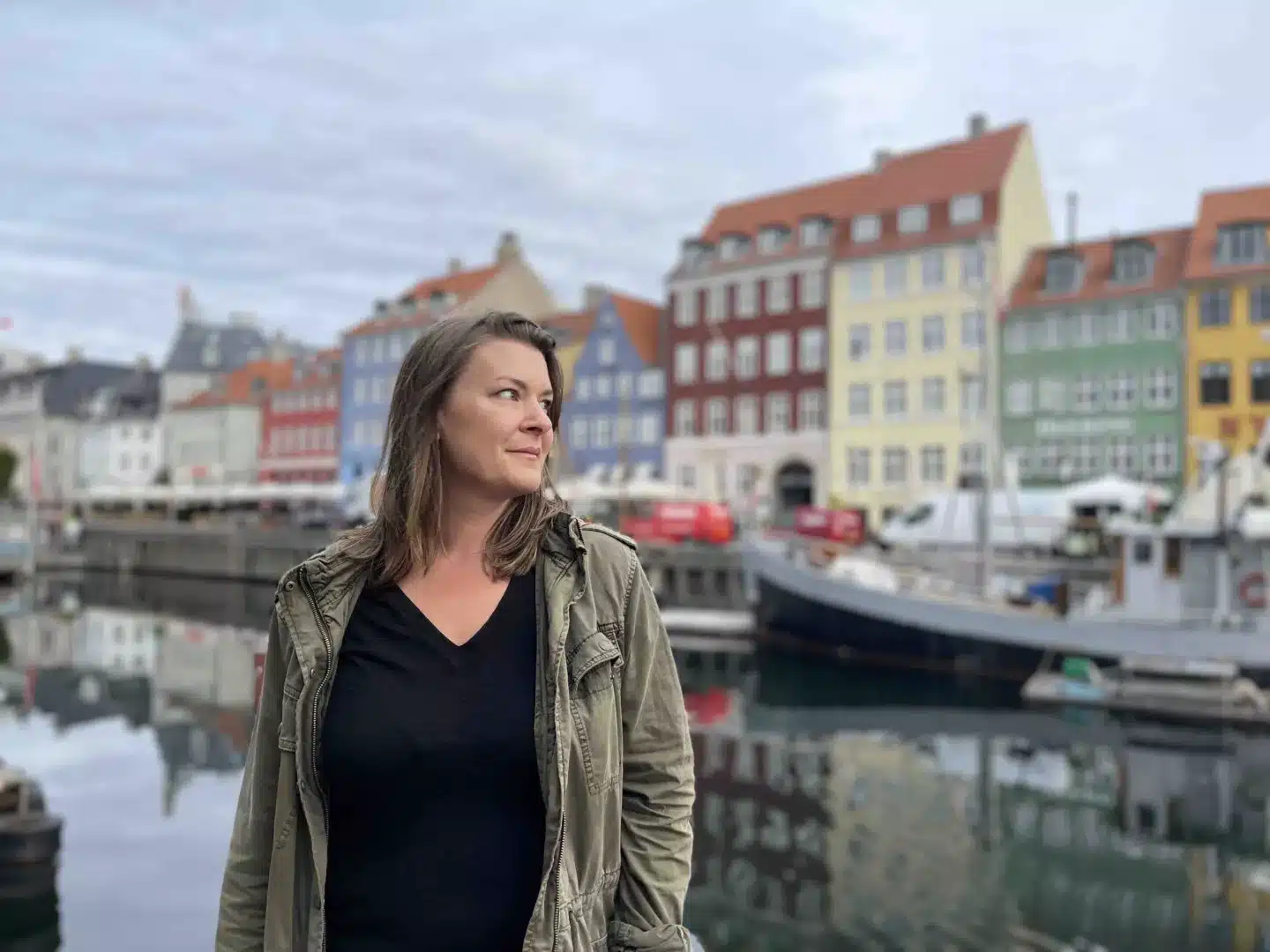 A woman alone in Denmark standing at the river with boats in the background. 